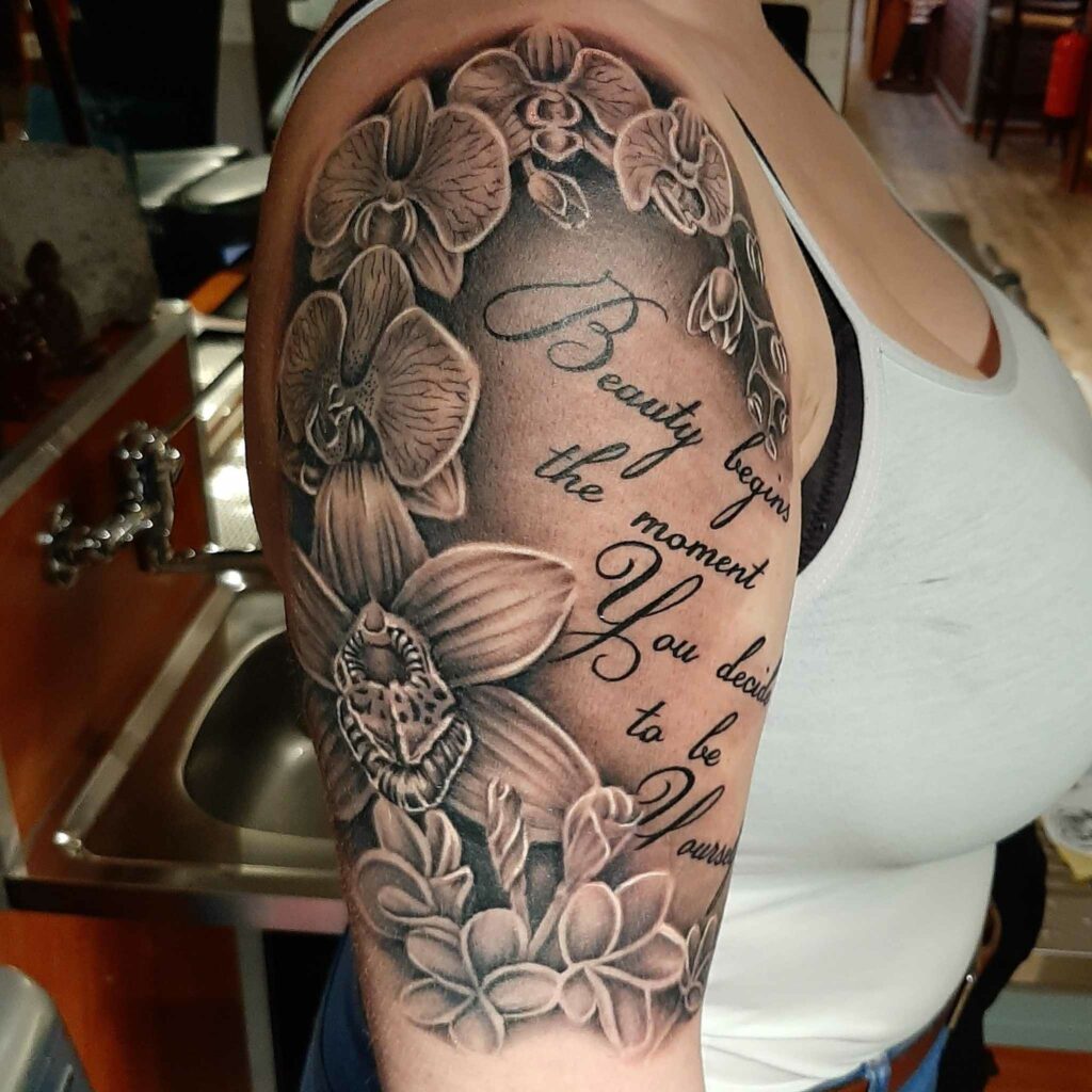 Zwart-grijze orchideeën en tekst 'Beauty begins...' op bovenarm.