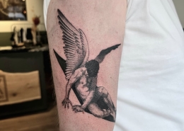 Zwart-wit tattoo van een gevallen engel op de bovenarm.