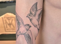 Twee vliegende zwaluwen in fineline en dotwork op de bovenarm.