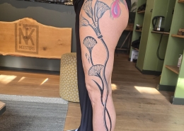 Grote fineline bloemen en een gekleurde veer op het bovenbeen.