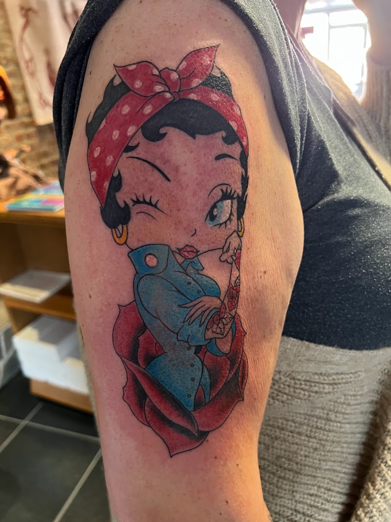 Kleurrijke Betty Boop pin-up tattoo in een rode roos op de bovenarm.