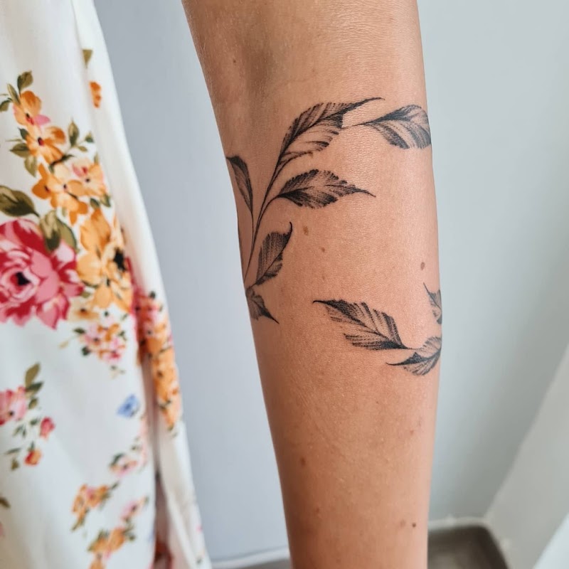 Fineline tattoo van een tak met bladeren die als een armband om de onderarm wikkelt.