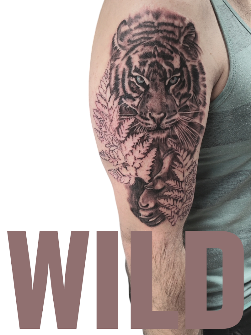 Realistische tijgerkop met blauwe ogen en varenbladeren op bovenarm.