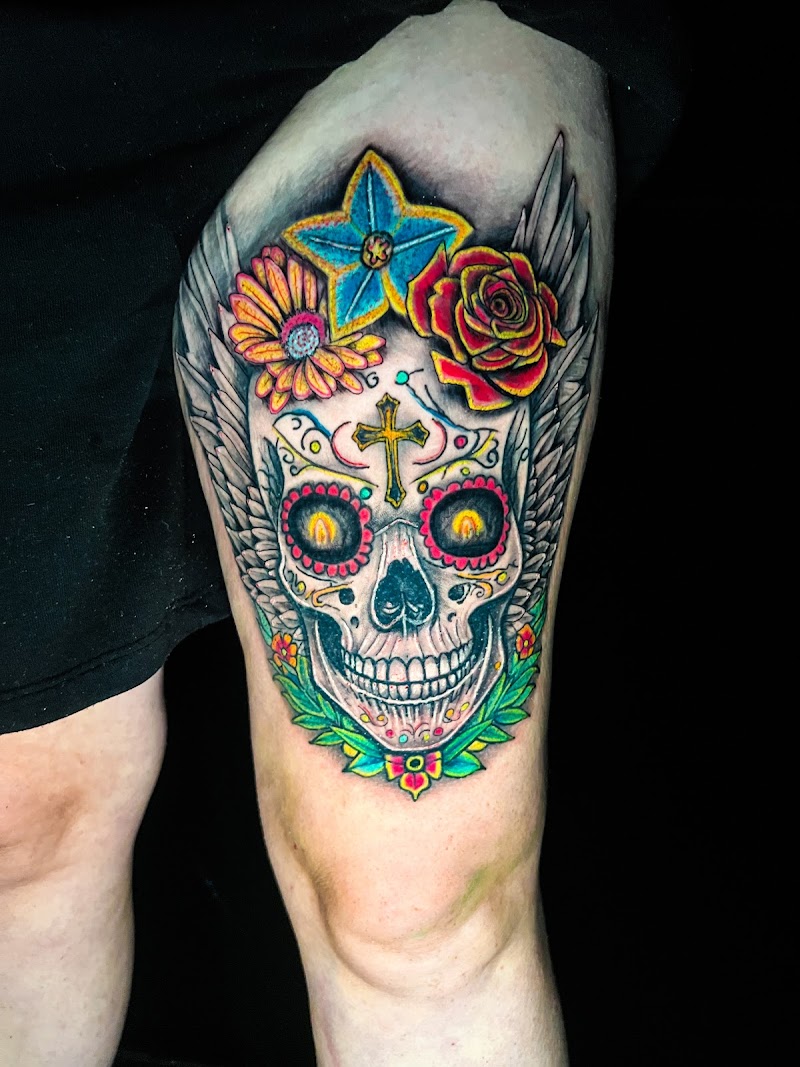 Kleurrijke sugar skull met vleugels, bloemen en een kruis op het bovenbeen.