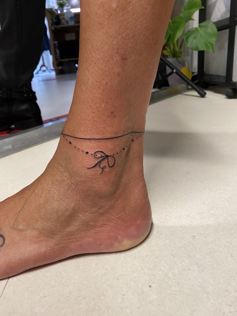 Fijne lijn enkelband tattoo met een klein strikje en stippen.