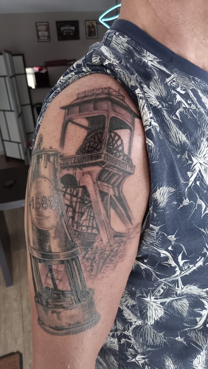 Zwart-wit tattoo van een mijnschacht en een mijnlamp op de bovenarm.