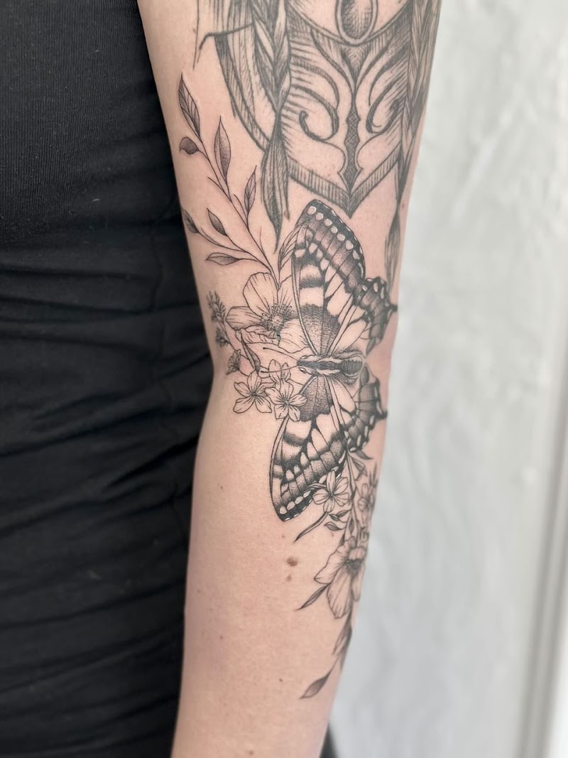 Zwart-wit vlinder met bloemen en bladeren op de bovenarm.