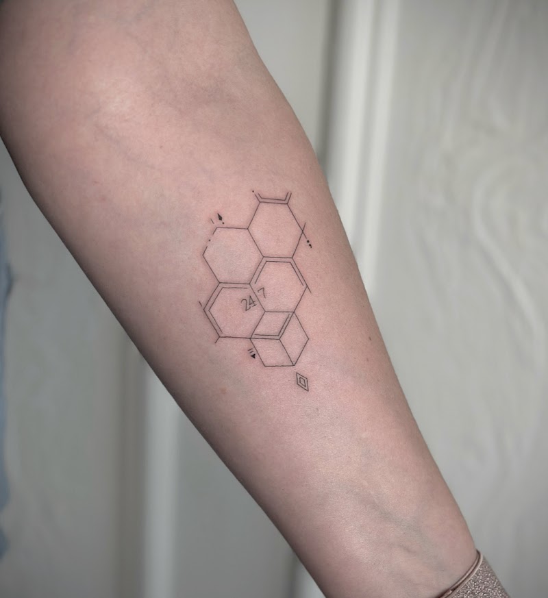 Fineline geometrische tattoo met honingraat en '24 7' op onderarm.