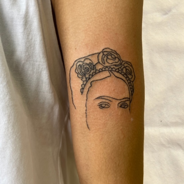 Minimalistische fineline tattoo van Frida Kahlo op de bovenarm.