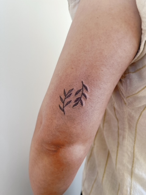 Twee kleine, minimalistische takjes met bladeren op de bovenarm.