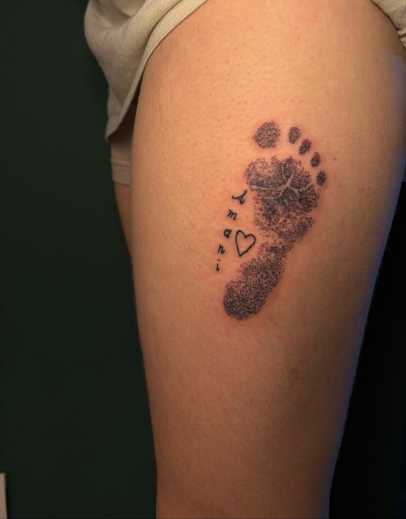 Dotwork voetafdruk met naam 'Amani' en hartje op bovenbeen.