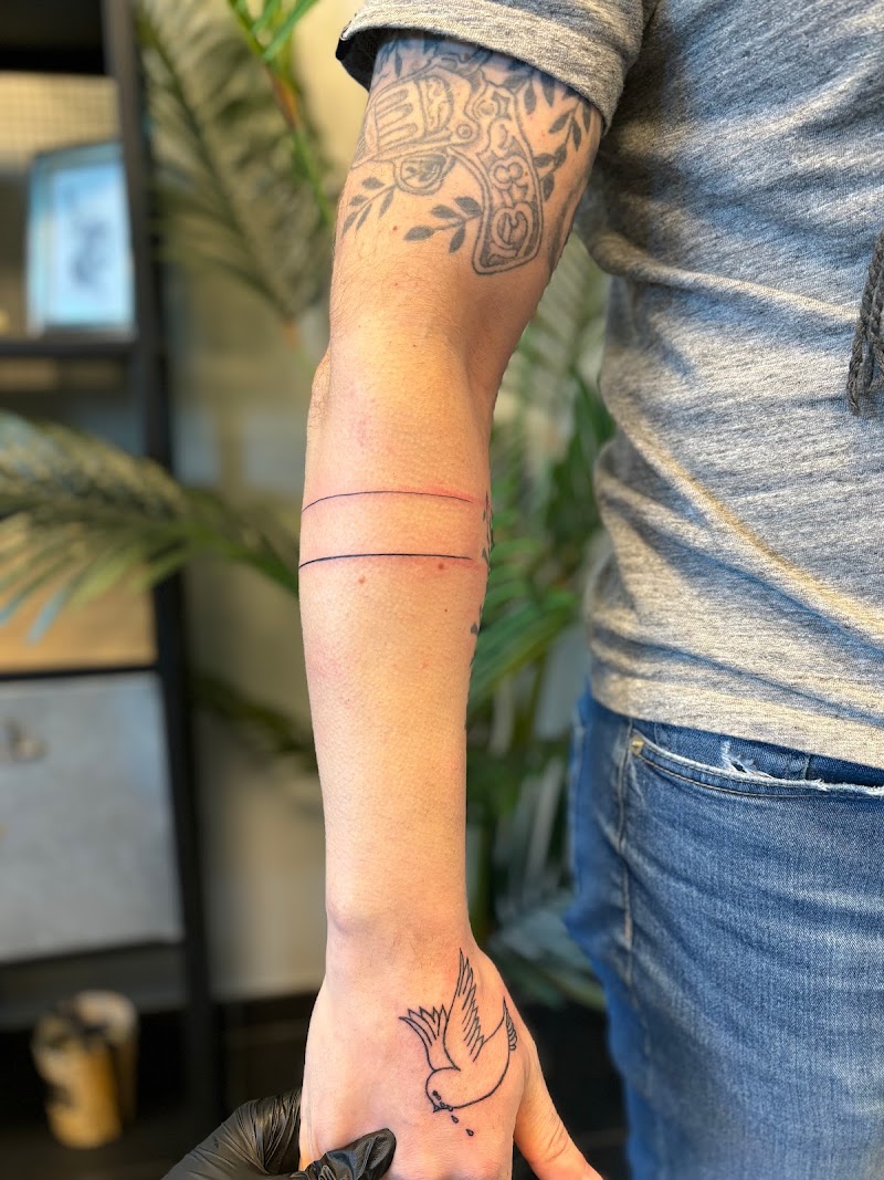 Arm met revolver, lijnenband en vogel tattoo in zwarte inkt.