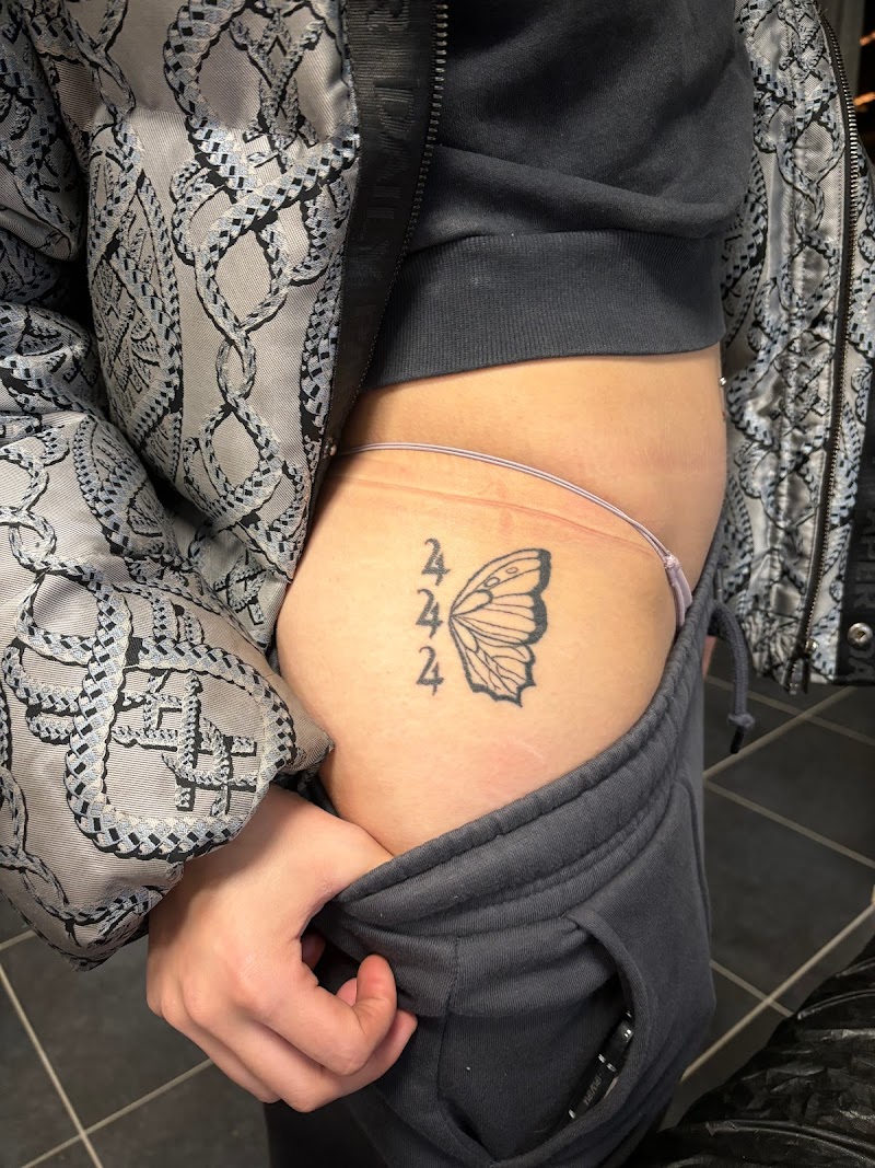 Zwart-wit tattoo van het getal 444 en een halve vlinder op de heup.