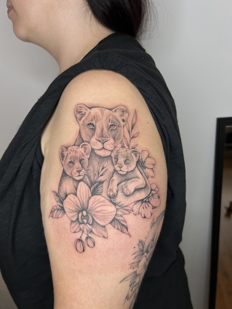 Fineline tattoo van leeuwin met twee welpjes en orchideeën op bovenarm.