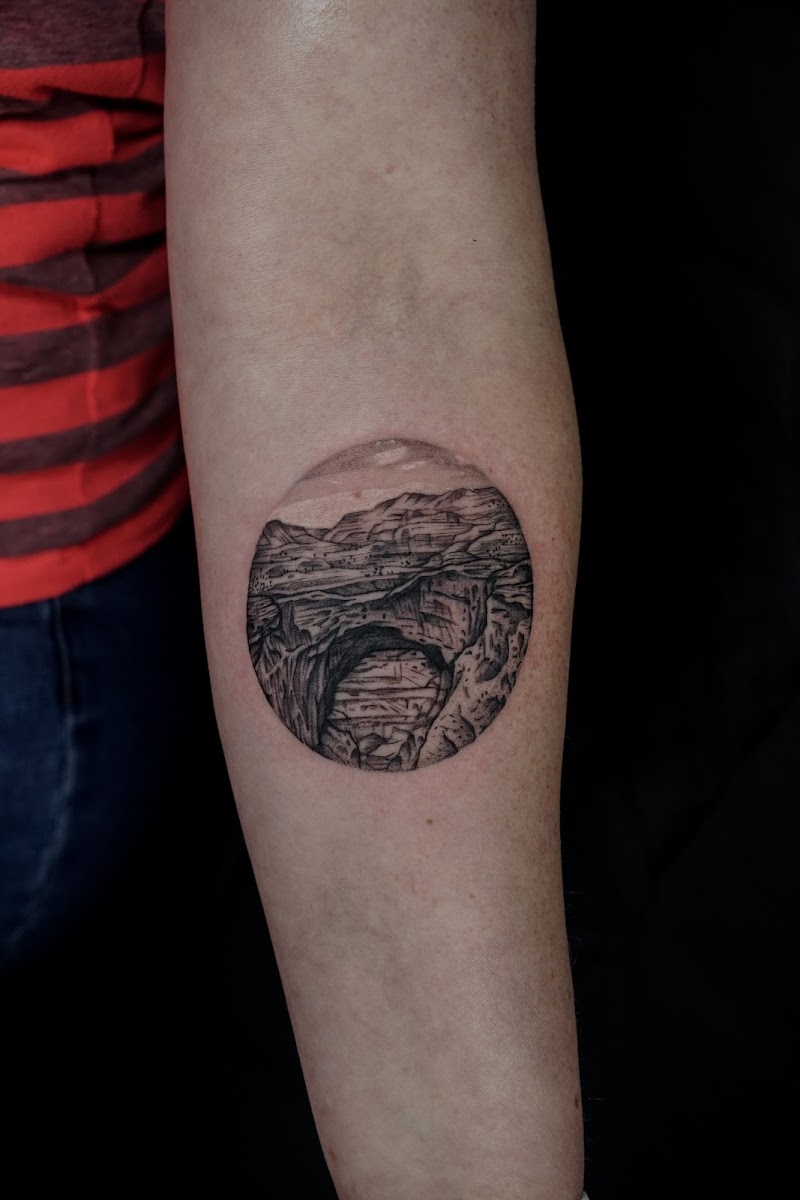 Cirkelvormige landschap tattoo van een canyon met een boog.