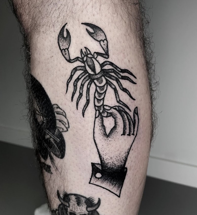 Hand die een schorpioen vasthoudt in blackwork stijl op het onderbeen.