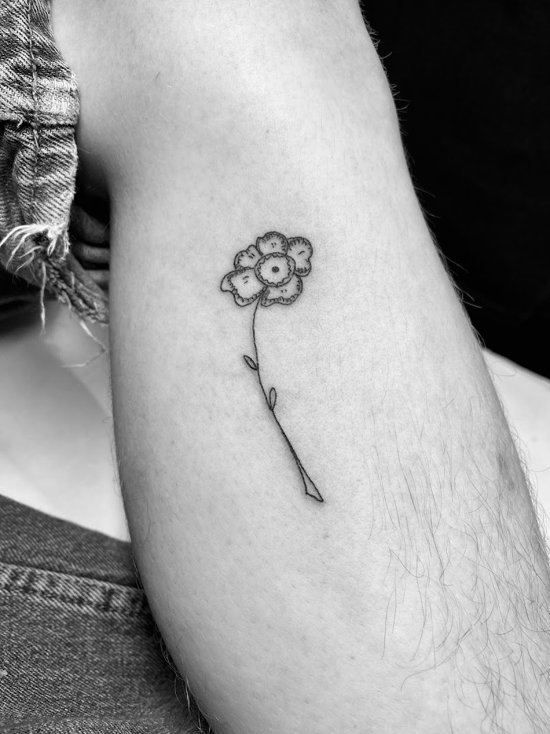 Kleine fineline bloem tattoo met een gezichtje in het hart op het onderbeen.