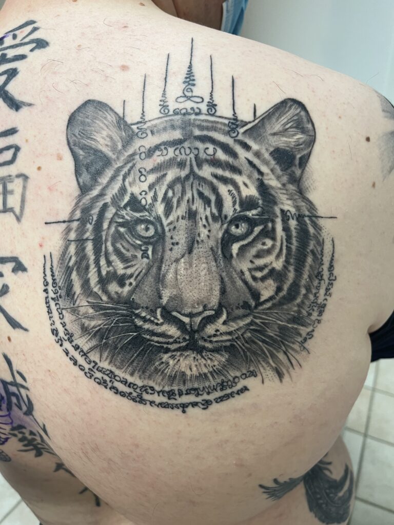 Realistische tijgerkop met Sak Yant symbolen op de bovenrug.