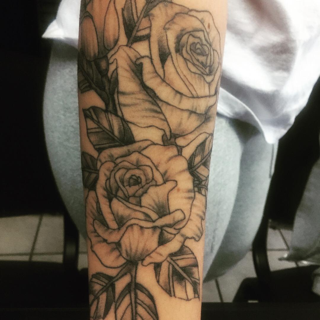 Zwart-wit fineline tattoo van rozen en bladeren op de onderarm.