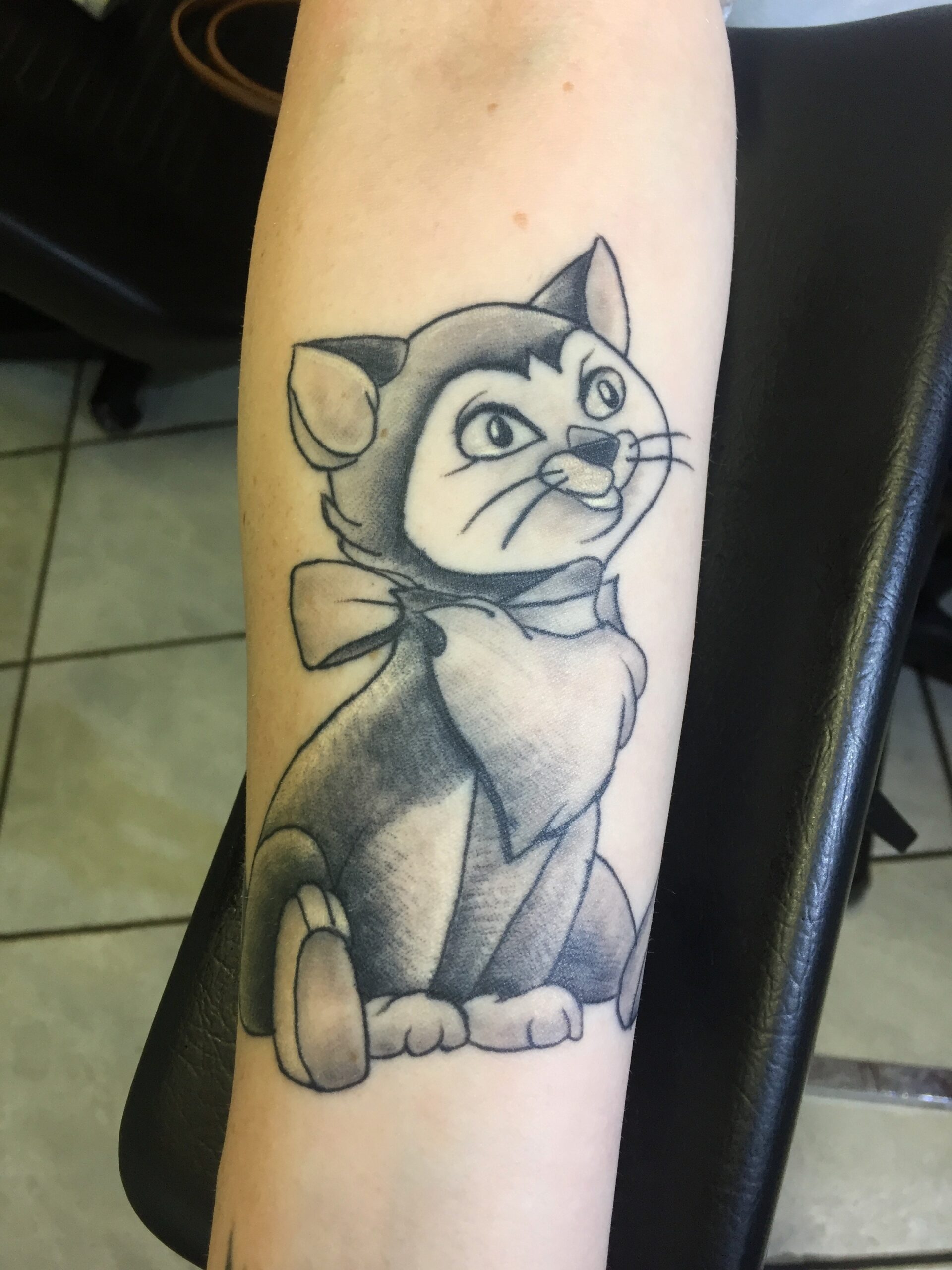 Zwart-wit tattoo van de kat Figaro uit Pinocchio op de onderarm.