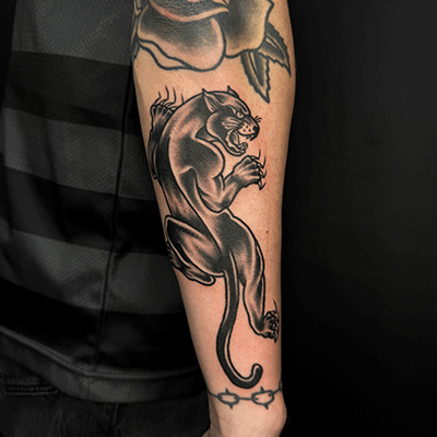 Zwart-witte traditionele panter tattoo op onderarm, met roos en prikkeldraad.