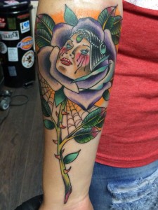 Neo-traditional tattoo van een vrouwenhoofd in een paarse roos met spinnenweb.