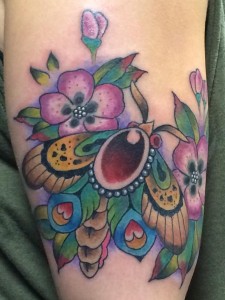 Kleurrijke neo-traditionele mot met bloemen op bovenarm.