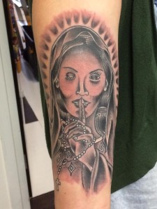 Zwart-wit tattoo van een gesluierde vrouw die 'ssst' zegt met een rozenkrans.