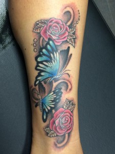 Tattoo van twee blauwe vlinders en twee roze rozen op het onderbeen.