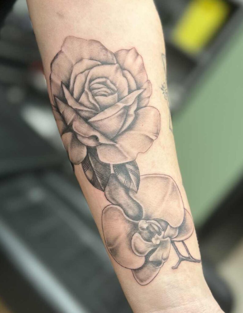 Zwart-wit tattoo van een roos en een orchidee op de onderarm.