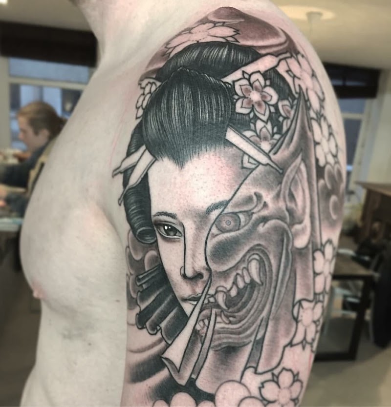 Zwart-wit tattoo van een geisha en Hannya masker op de bovenarm.
