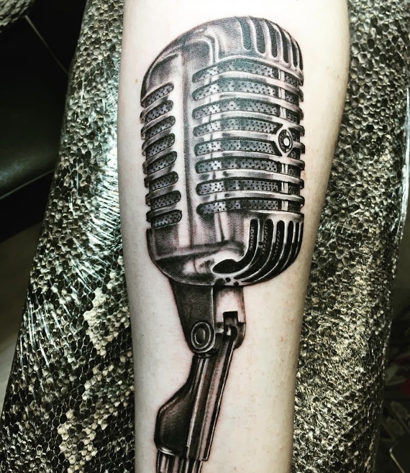 Realistische zwart-wit tattoo van een vintage microfoon op de onderarm.