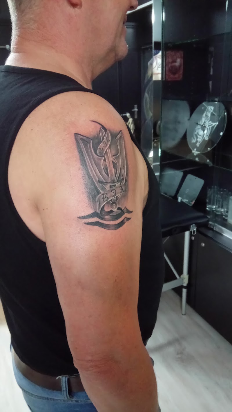 Zwart-wit tattoo van een anker met een drietand en een lint met tekst op de bovenarm.