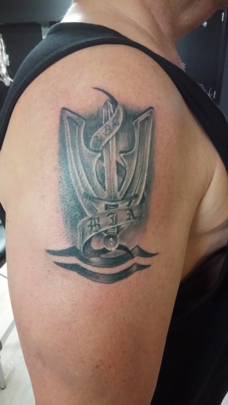 Zwart-wit embleem tattoo met zwaard, lint en de letters 'BJA' op de bovenarm.
