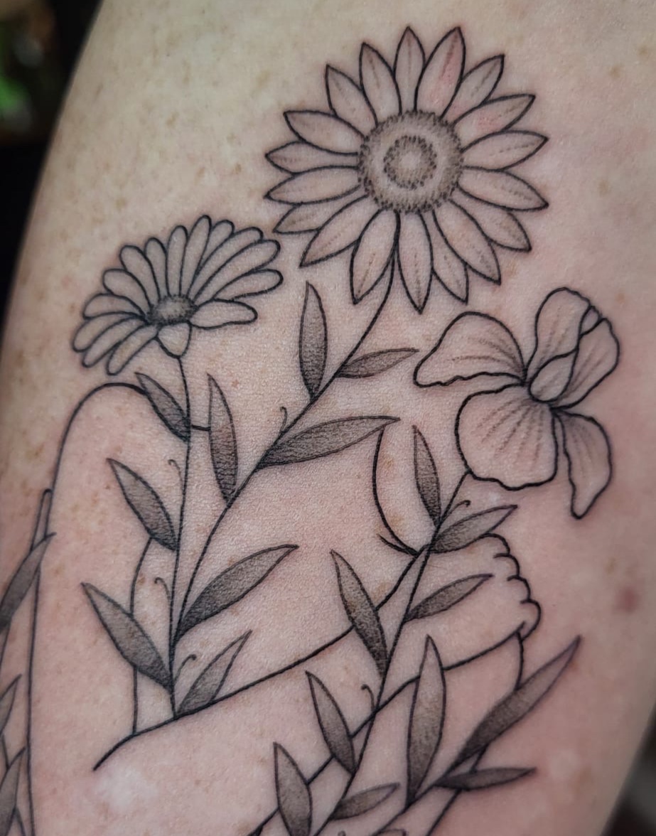 Fineline tattoo van drie bloemen (zonnebloem, iris, madeliefje) in zwart-wit.