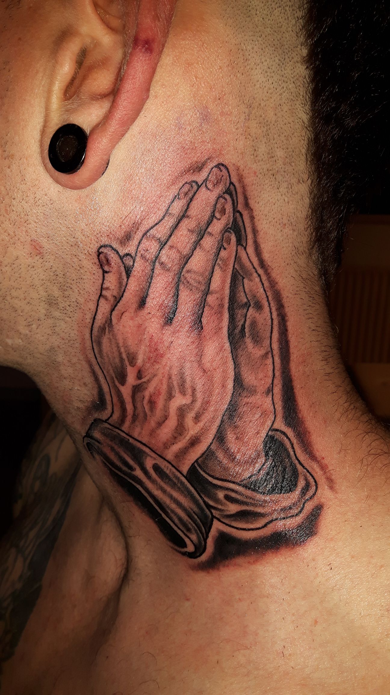 Zwart-wit tattoo van biddende handen op de nek.