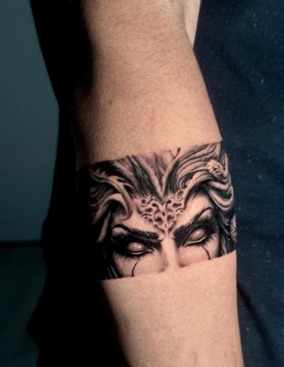 Realistische zwart-wit tattoo van Medusa's ogen en slangenhaar in een band.