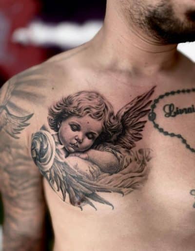Realistische zwart-wit tattoo van een slapende cherubijn op de borst.