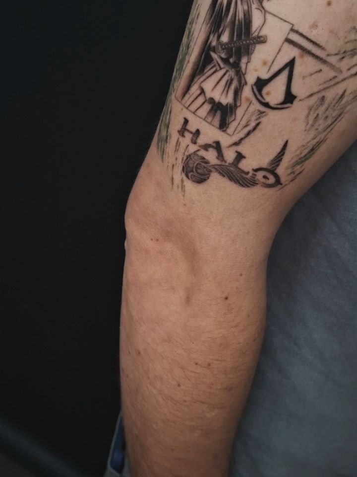 Gaming tattoo met Assassin's Creed logo, Halo tekst en figuur.