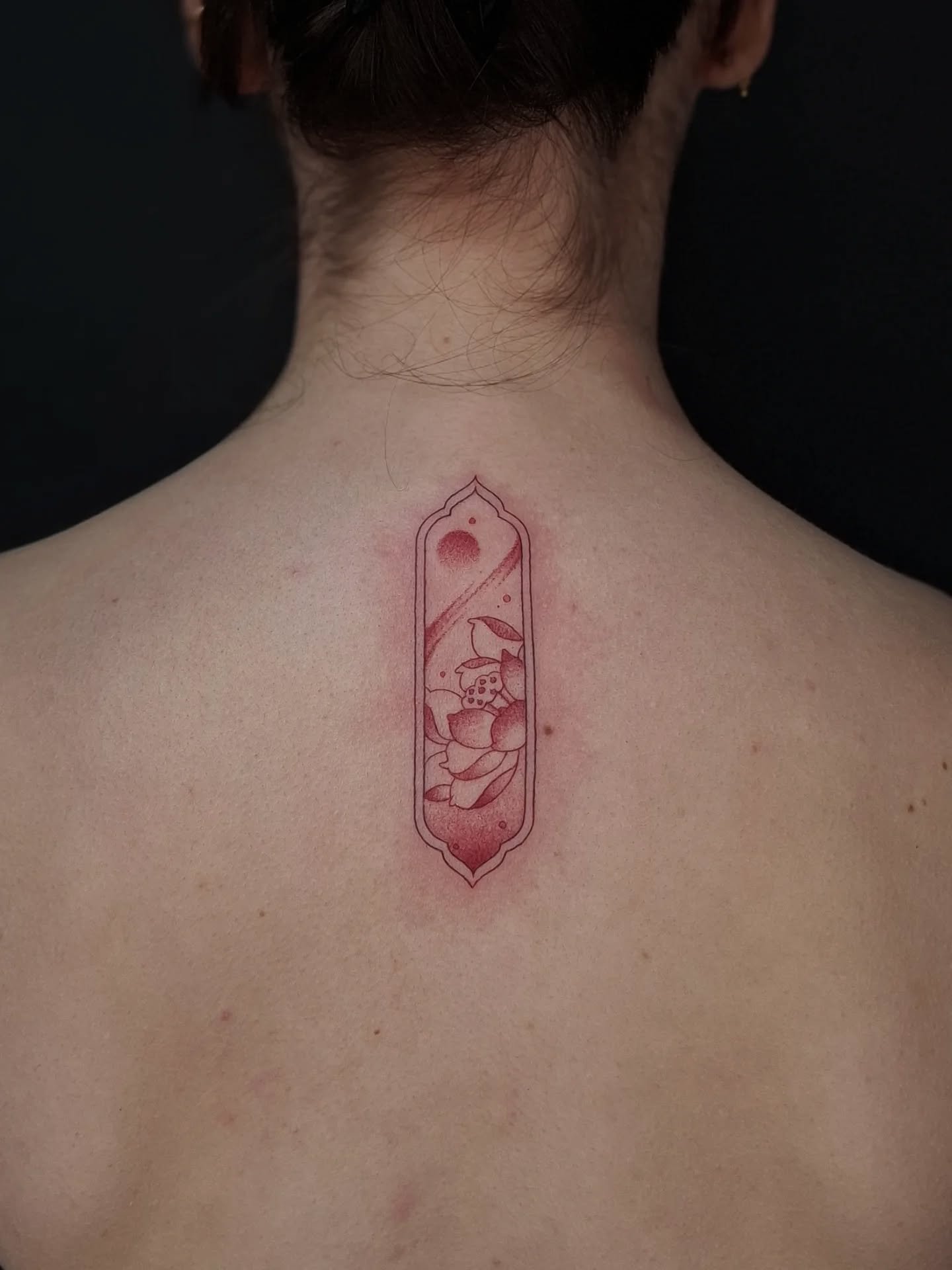 Rode fineline lotus in een sierlijk kader op de nek.