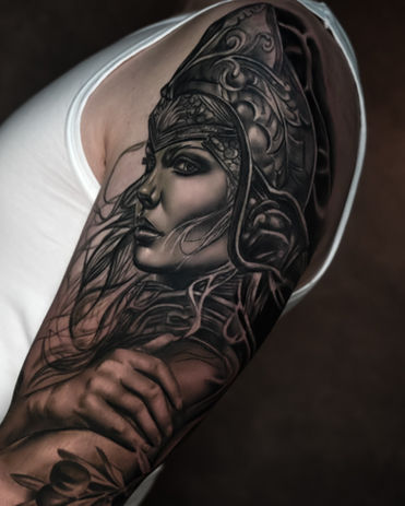 Realistische zwart-wit tattoo van een vrouwelijke krijger met helm op bovenarm.