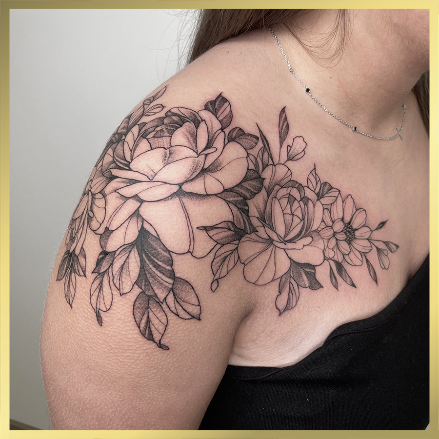 Elegante zwart-wit bloemen tattoo op schouder en sleutelbeen.