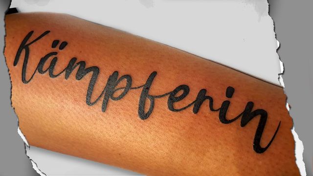 Zwart 'Kämpferin' woord in sierlijk handschrift op onderarm.