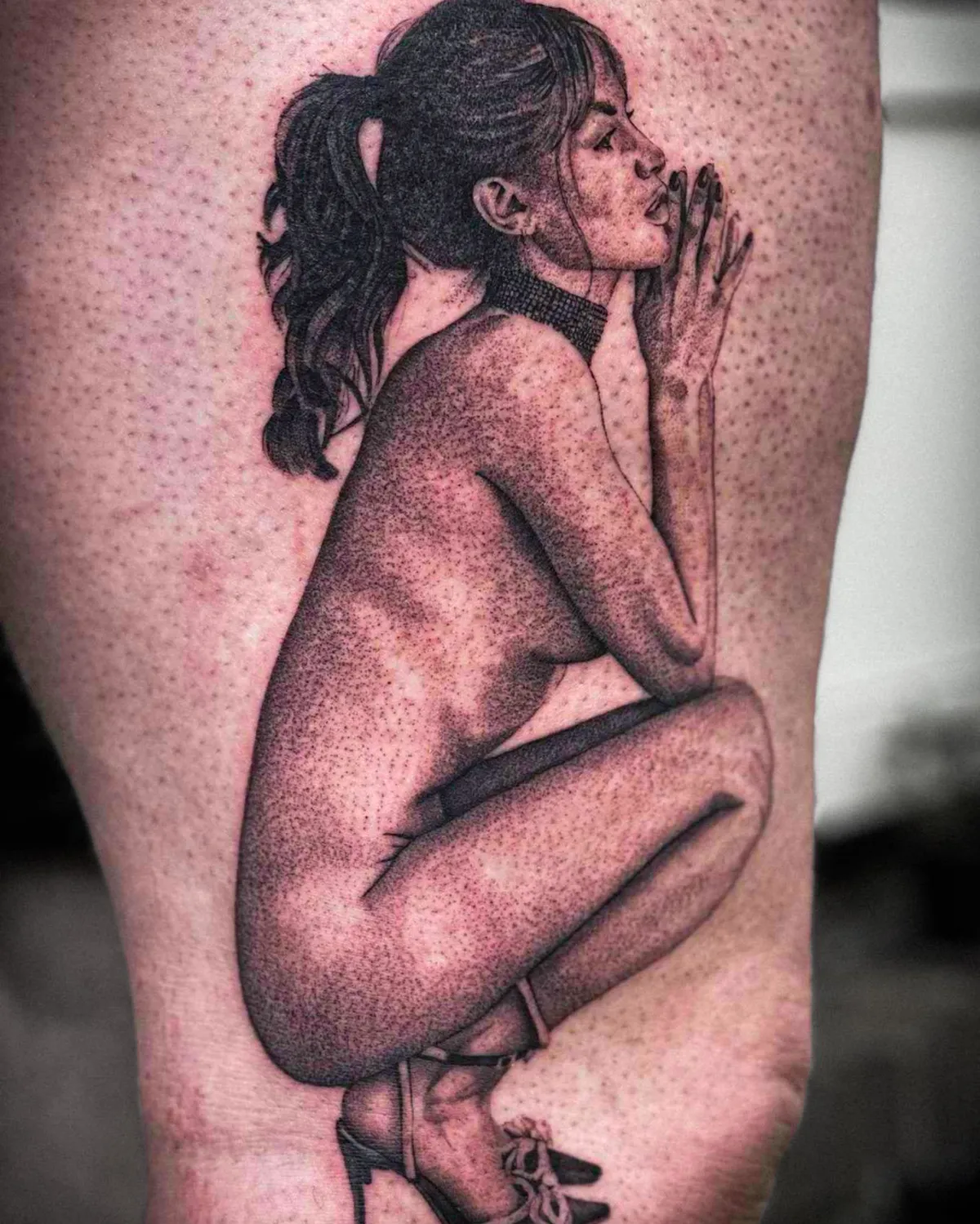 Zwart-wit dotwork tattoo van een hurkende naakte vrouw met paardenstaart en hakken.