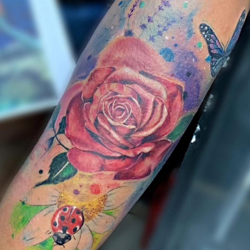 Kleurrijke watercolor tattoo van een roos, lieveheersbeestje en vlinder.