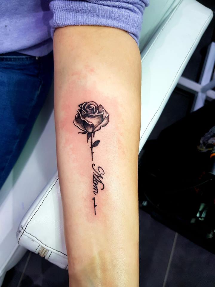 Zwart-witte roos met 'Mom' in sierlijk schrift op de onderarm.
