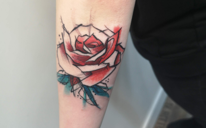 Abstracte roos tattoo met rode en blauwe waterverf effecten op de onderarm.