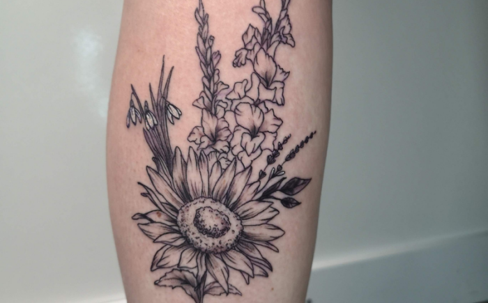 Zwart-wit tattoo van een bloemenboeket met zonnebloem, gladiolen en sneeuwklokjes.