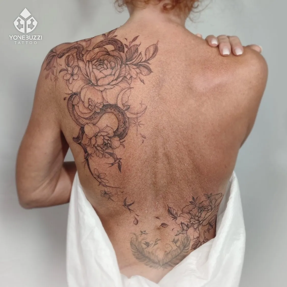 Grote rugtattoo met slang, pioenrozen, vlinders en maan in fineline stijl.