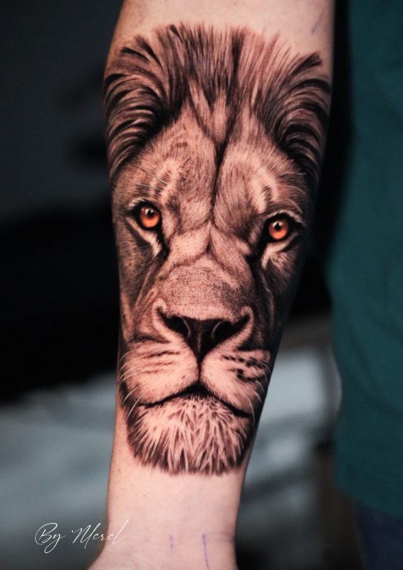 Realistisch leeuwenportret met oranje ogen op onderarm.